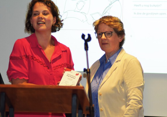 Foto van ECAL directeur Femia Siero waarop ze het 1e exemplaar van het Veluwse zorgzakboekje overhandigt aan WZU zorgmedewerkster Ellen Kroon